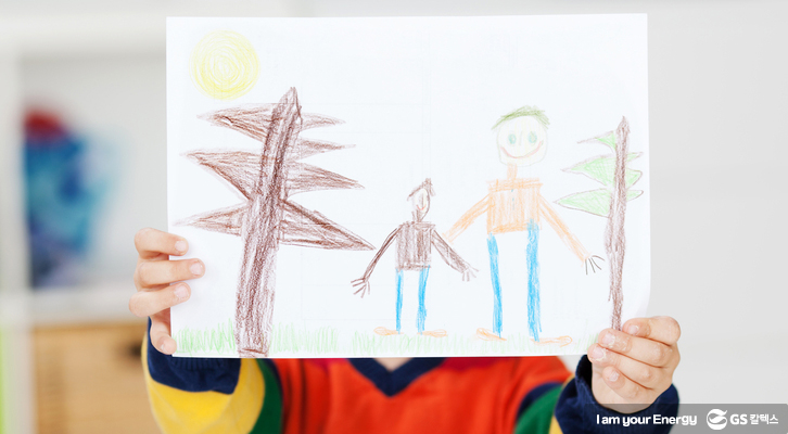 아이가 자신의 그림을 들고 서 있다.