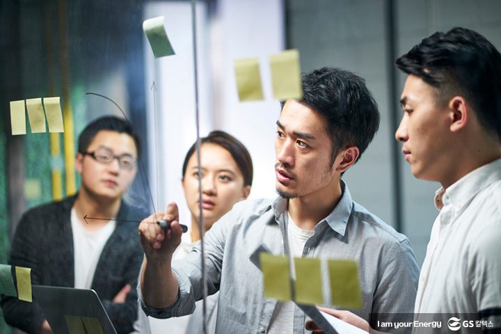 회사 사원들이 투명보드에 글을 쓰며 회의하고 있는 모습